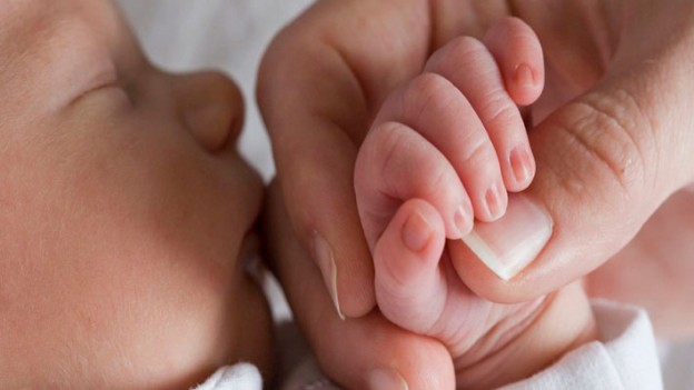 Hermoso bebé recién nacido con los ojos cerrados junto a la mano de su madre